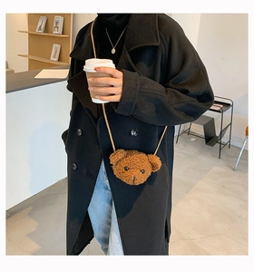 Detail shot of brown plush bear crossbody bag worn by a model in a black coat