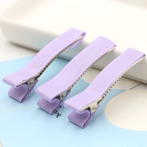 Macro shot of three purple ribbed ribbon duckbill hair clips with clear texture on tray