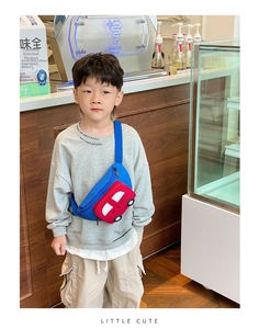 Detail of red car-shaped kids chest bag in blue canvas with adjustable strap on boy