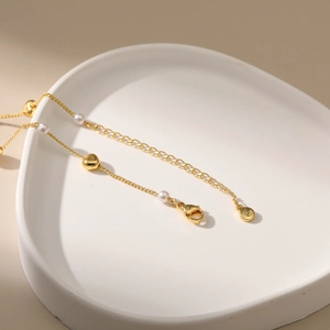 Elegante goldene Herz-Halskette mit Perlen auf einem minimalistischen weißen Tablett