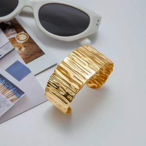 Golden wide open cuff bracelet with rippled wave texture on a minimalist white display