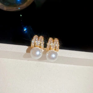 Macro view of gold letter M stud earrings with sparkling zircons and white pearl drop