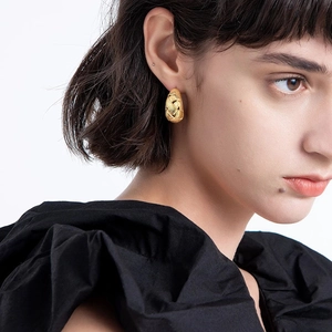 Close-up of woman wearing golden woven teardrop earrings with a textured mesh design