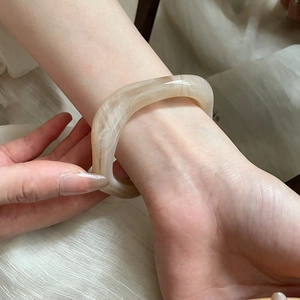 Close-up of irregular marbled cream resin open bangle on wrist with fabric background