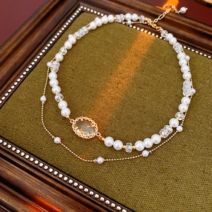 Double-layered gold necklace with faux pearls and emerald gemstone pendant on velvet