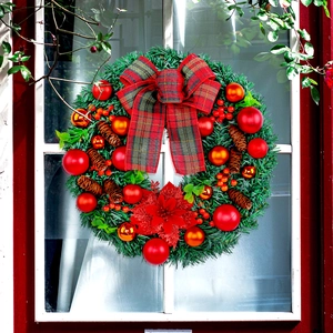 Christmas wreath with red bow, pine cones and berries hanging on a white window frame