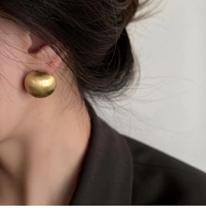 Close-up of minimalist matte gold geometric stud earring on model with textured finish