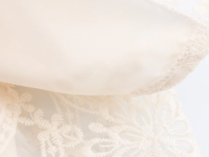 Macro shot of elegant beige lace embroidery and satin fabric texture on a tiered maxi dress