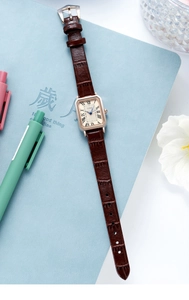Detail of square rose gold watch with brown leather strap on a blue notebook