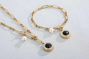 Detail of gold necklace and bracelet set with white pearl and black round gemstone charms