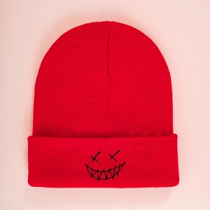 Detailed close-up of red knit beanie featuring black embroidered smiley face patch
