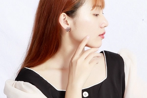 Close-up of silver-toned round stud earring with embossed logo on a female model