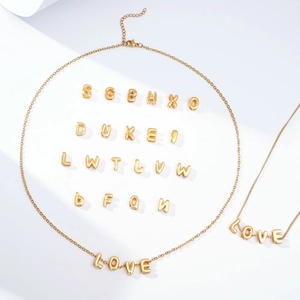 Detailed view of gold bubble letter pendants and layered necklaces on a white background
