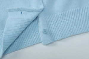 Detailed macro view of light blue knitted cardigan hem with matching resin button detail
