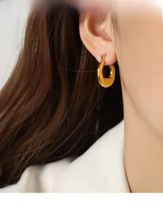 Macro detail of glossy gold plated chunky oval hoop earring on female model