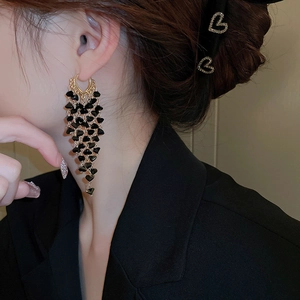 Detail of gold hoop earring with black heart crystal tassel worn by a model in a black suit