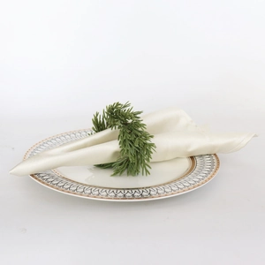 Detail of a green pine needle napkin ring on a beige silk napkin with white ceramic plate