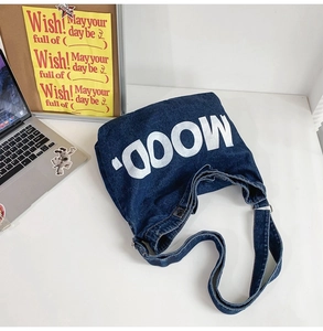 Detailed top view of a dark blue denim shoulder bag with MOOD lettering on a desk