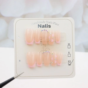 Close-up of handmade pink French press-on nails with heart patterns and small rhinestones