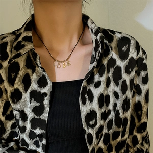 Close-up of gold LOVE pendant on a thin black cord necklace worn by a model