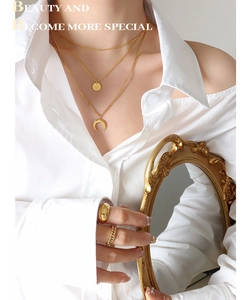 Detail of layered gold necklaces with crescent and star pendants worn with a white shirt