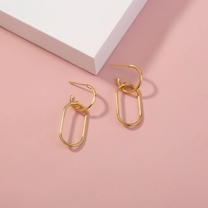 Elegant gold-plated geometric drop earrings with long oval pendants on pink background
