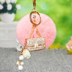 Detail of pink faux fur pompom keychain with gold rhinestone bag charm and white rose pearl
