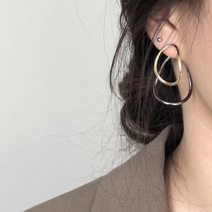 Detail of elegant contrasting gold and silver oval earrings worn on model's ear