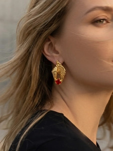 Detailed close-up of a luxury gold seashell earring with a red gemstone on a model
