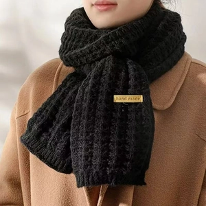 Thick black knitted scarf with handmade yellow label styled over a wool coat
