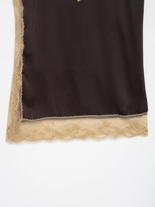 Close-up of brown satin fabric with intricate gold eyelash lace trim on the hemline