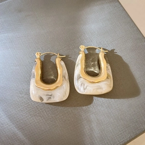 Détail de boucles d'oreilles dorées en U avec résine marbrée blanche sur fond noir