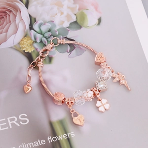 Detail of rose gold snake chain bracelet with heart, clover, and floral charms