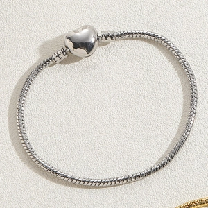 Macro detail of silver heart clasp on snake chain bracelet with polished metallic finish