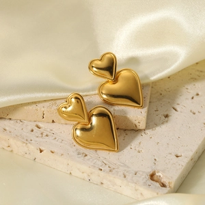 Golden double heart earrings made of stainless steel displayed on a textured stone base