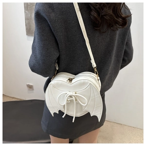 Rear view of a model wearing a white heart-shaped bag with bat wings and cross-strap details