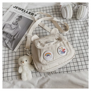 Close-up of cream canvas crossbody bag featuring cute bear badges and plush bear charm