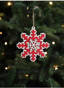 Close-up of a red and white wooden snowflake ornament hanging on a Christmas tree branch