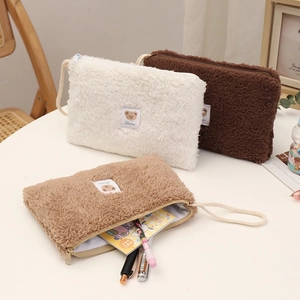 Détail de trois trousses à maquillage en peluche crème, marron et kaki avec logo ours