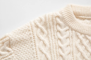 Dettaglio del maglione a trecce color panna con scollo a girocollo e trama a nido d'ape