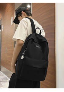 Rear view of a black canvas backpack with white embroidery and astronaut charm on a model