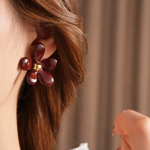 Detail of dark red floral earrings with golden center worn by a female model