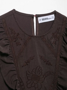 Détail de la broderie florale sur l'encolure d'une chemise marron avec volants