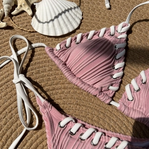 Detail of pink ribbed bikini top with white woven straps and silver eyelets on beach mat