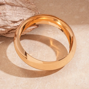 Close-up of a wide polished gold metal cuff bracelet with elegant twist detail on marble