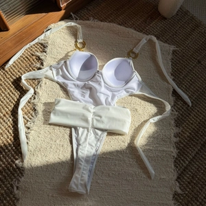 Detail of white swimsuit featuring gold metal rings and pleated waist belt on a textured rug