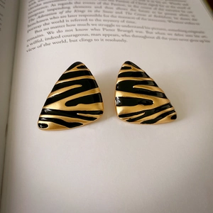 Vintage irregular earrings with black and gold enamel stripes on an open book