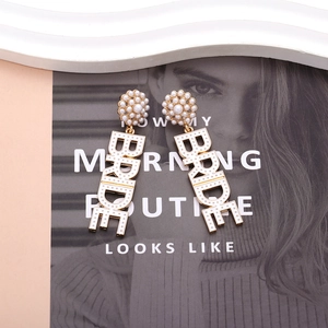 Golden bridal earrings with white pearls and hanging BRIDE letters on stone background