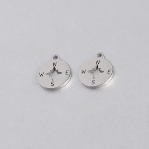 Close-up of silver stainless steel compass charms with hollowed-out NESW directional letters