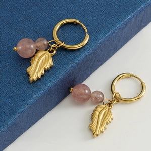 Macro detail of gold-plated leaf earring with natural pink stone on jewelry box